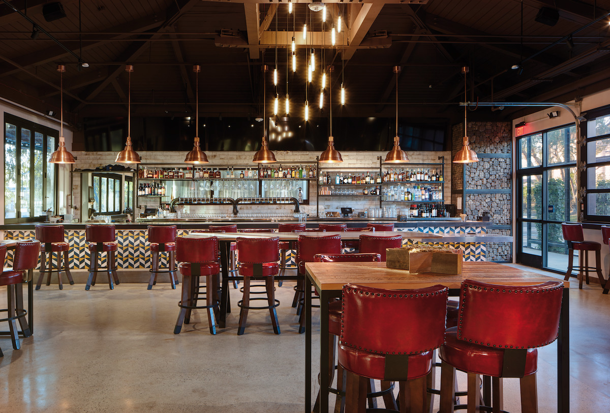 photo inside Oscar's Brewing Company's bar in Temecula with red leather high top bar stools + tables and barter overlooking the bar with liquor bottles on the shelves