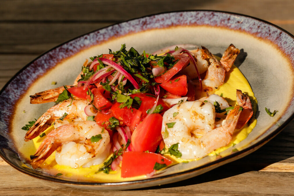 a plate of food with shrimp, tomatoes, onions, and cilantro on top with a yellow sauce underneath