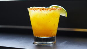 up close shot of a mango margarita on the rocks with a tajin rim and lime wedge