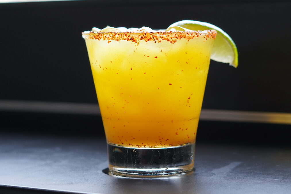 up close shot of a mango margarita on the rocks with a tajin rim and lime wedge