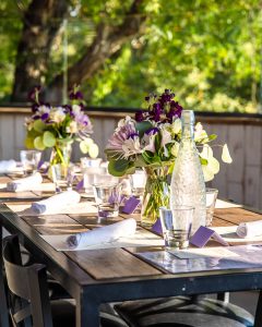 A restaurant table set with a fresh floral centerpiece and place settings on an outdoor patio.