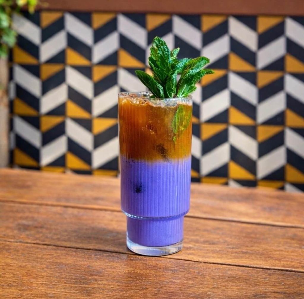 A colorful layered cocktail garnished with fresh mint, served on a wooden table.