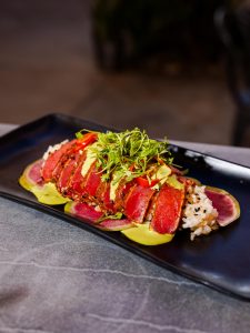 A plated seared tuna entrée served over rice with fresh vegetables and garnishes.